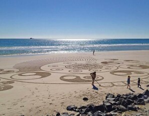A beach with a large sand drawing and rocks in the foreground. - Byron Bay Beach Apartment BELONGIL BEACH (Byron Bay)