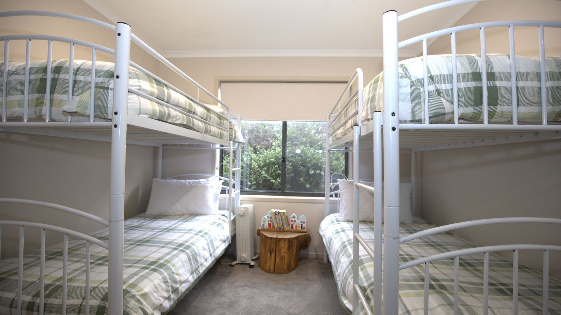 Een studentenkamer met stapelbedden, een klein houten tafeltje en een raam met uitzicht op bomen.