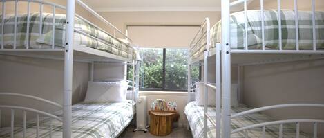 Een studentenkamer met stapelbedden, een klein houten tafeltje en een raam met uitzicht op bomen.