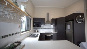 A modern kitchen with dark cabinets, a stainless steel refrigerator, a microwave, and a sink. - Boronia - 7/30 Nettin Circuit (Jindabyne)