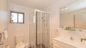 Een moderne badkamer met een douchecabine van glas, een toilet, een wastafel met spiegel en een klein raam boven het toilet.