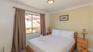 Une chambre à coucher comprenant un lit, deux tables de chevet, une fenêtre avec des rideaux, un tableau accroché au mur et un radiateur.