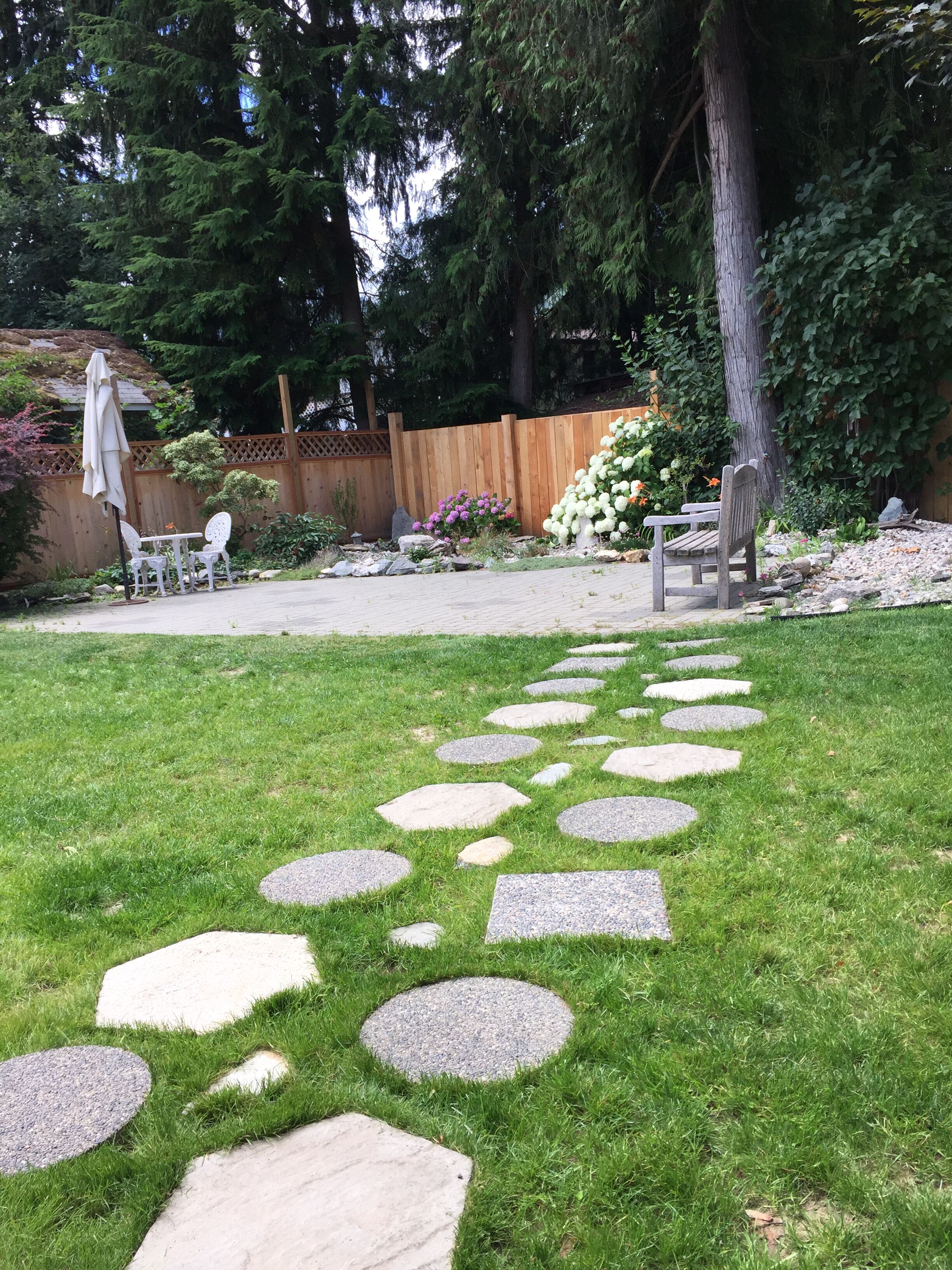 A garden with a stone pathway leading to a wooden bench and a table with chairs.