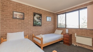 A room with two wooden beds, a brick wall, a large window, and a radiator. - Lodge 67 - 3/58 Townsend Street (Jindabyne)