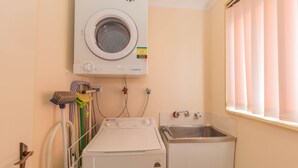 A laundry room with a front-loading washer and dryer, a sink, and a window with blinds. - Lodge 67 - 3/58 Townsend Street (Jindabyne)