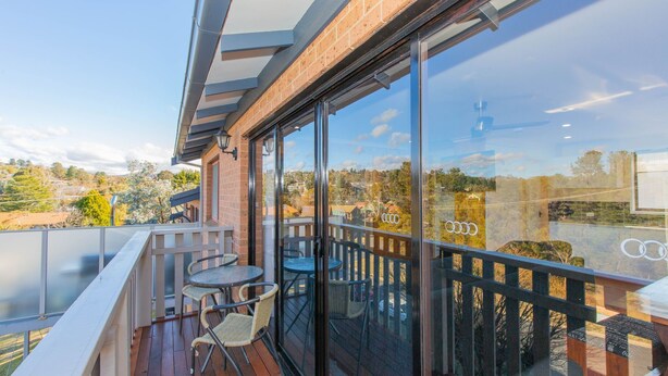 A balcony with a glass door, wicker chairs, and a small round table. - Lodge 67 - 3/58 Townsend Street (Jindabyne)