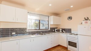 A modern kitchen with white cabinets, a black tiled backsplash, a window, a microwave, a stove, and a refrigerator. - Lodge 67 - 3/58 Townsend Street (Jindabyne)