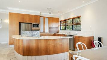 A modern kitchen with wooden cabinetry, a central island, stainless steel appliances, and a window with blinds.
