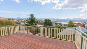 Een houten terras met een groene balustrade, met uitzicht op een woongebied met huizen en een meer.