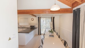 Een moderne keuken met een houten plafond, een eethoek met een lange tafel en stoelen, en een raam met jaloezieën.