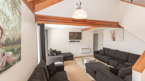 Een moderne woonkamer met donkergrijze banken, een ronde salontafel en een groot schilderij van een boslandschap.