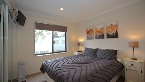 A bedroom with a large bed, a window, a bedside table with a lamp, and three wall-mounted paintings.