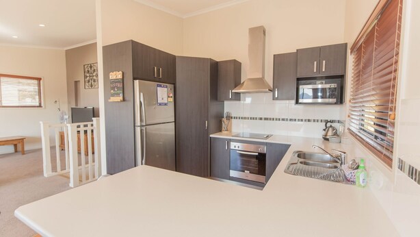 A modern kitchen with dark cabinets, a stainless steel refrigerator, a microwave, and a built-in oven.