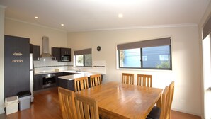 A modern kitchen with dark cabinets, a microwave, and a stove. There is a wooden dining table with chairs. A clock is on the wall, and a window provides natural light.