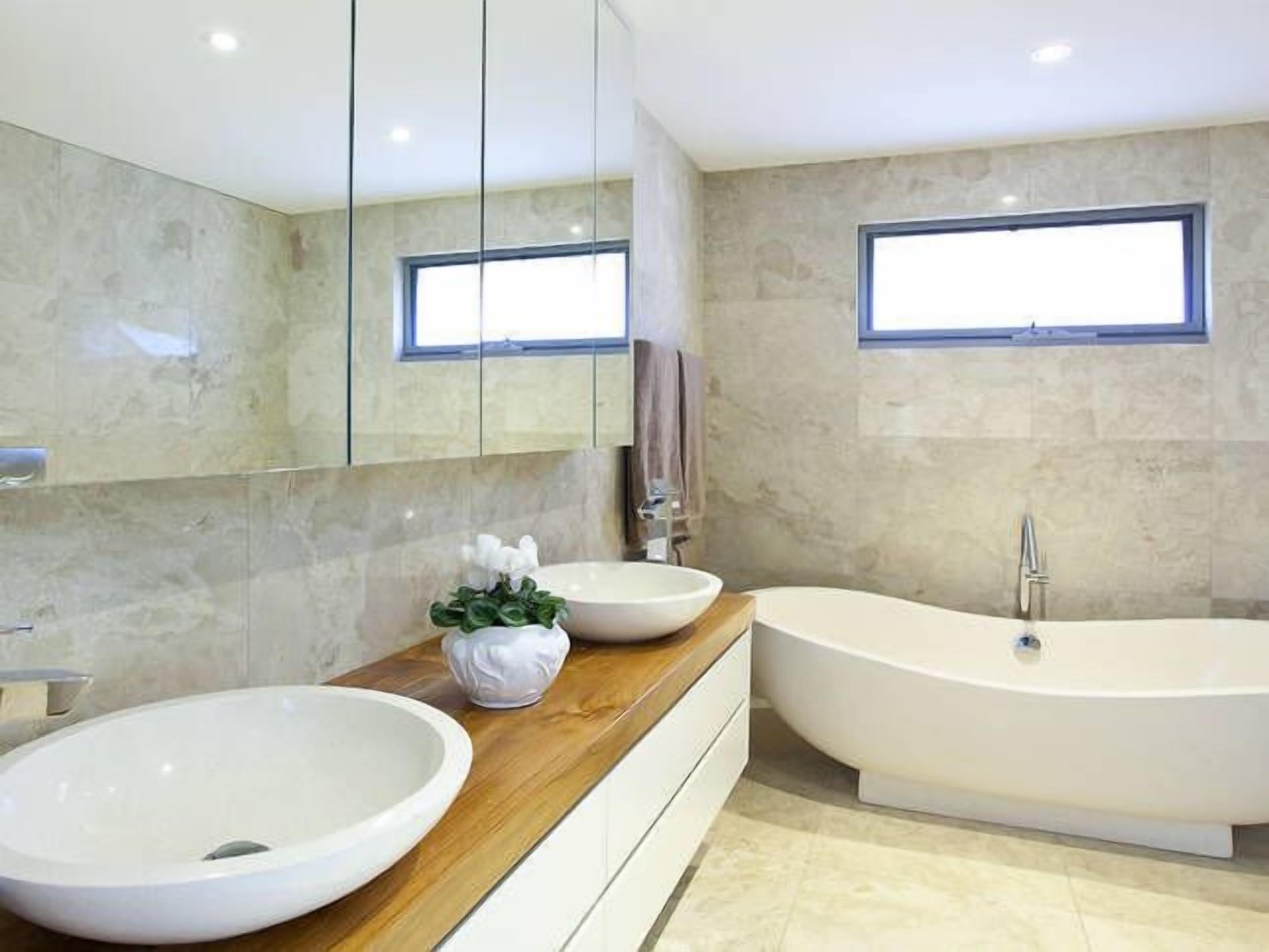 Ein modernes Badezimmer mit einer großzügigen freistehenden Badewanne, einem Vessel-Becken und einem großen Spiegel.