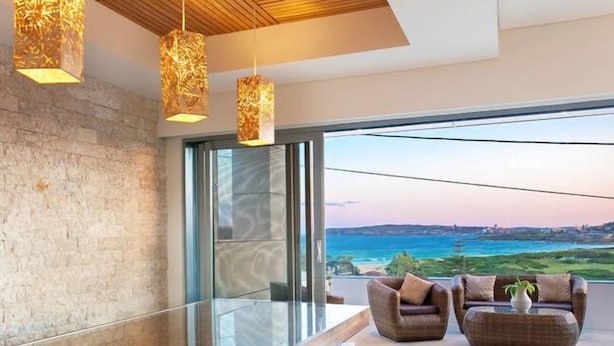 A modern interior with a glass partition, wicker furniture, and a view of the sea. - Luxury Beach Home Pool Ocean Views Walk to Beach (North Curl Curl)