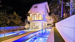 A modern two-story house with a swimming pool, surrounded by a fence and palm trees. - Luxury Beach Home Pool Ocean Views Walk to Beach (North Curl Curl)