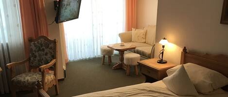 A hotel room with a wooden bed, a chair, a small table, and a television on the wall.