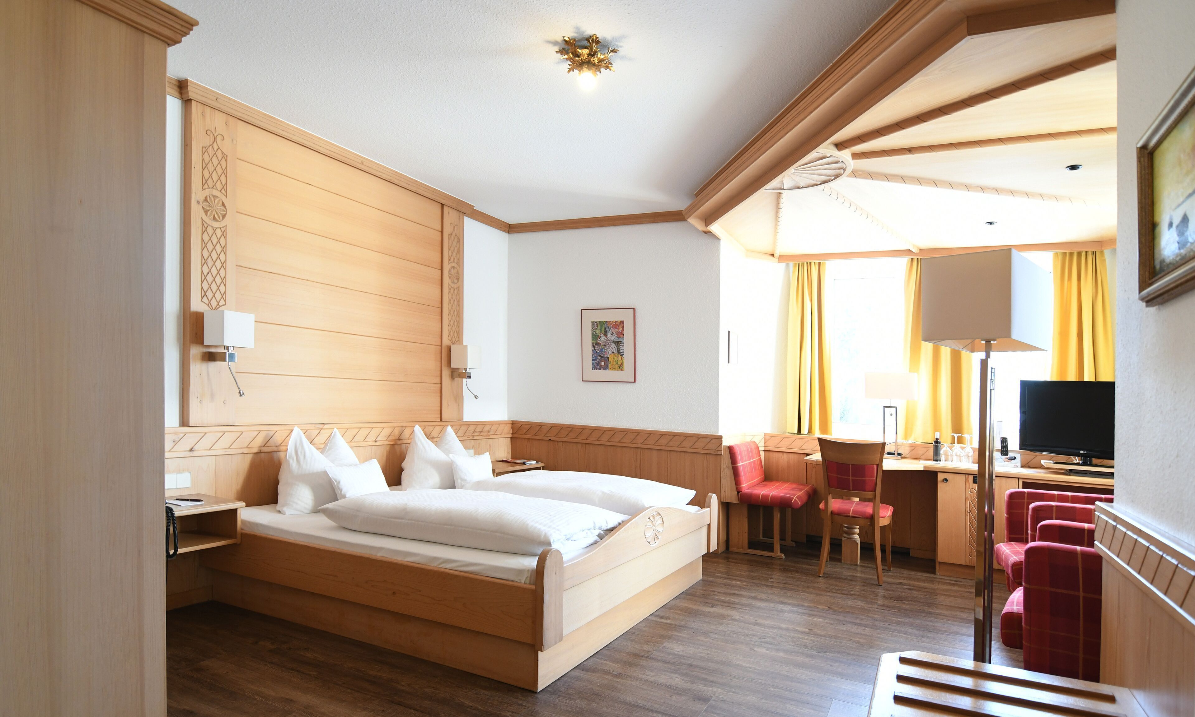 Een hotelkamer met een houten bed, een bureau met stoel, een televisie en een raam met gordijnen.