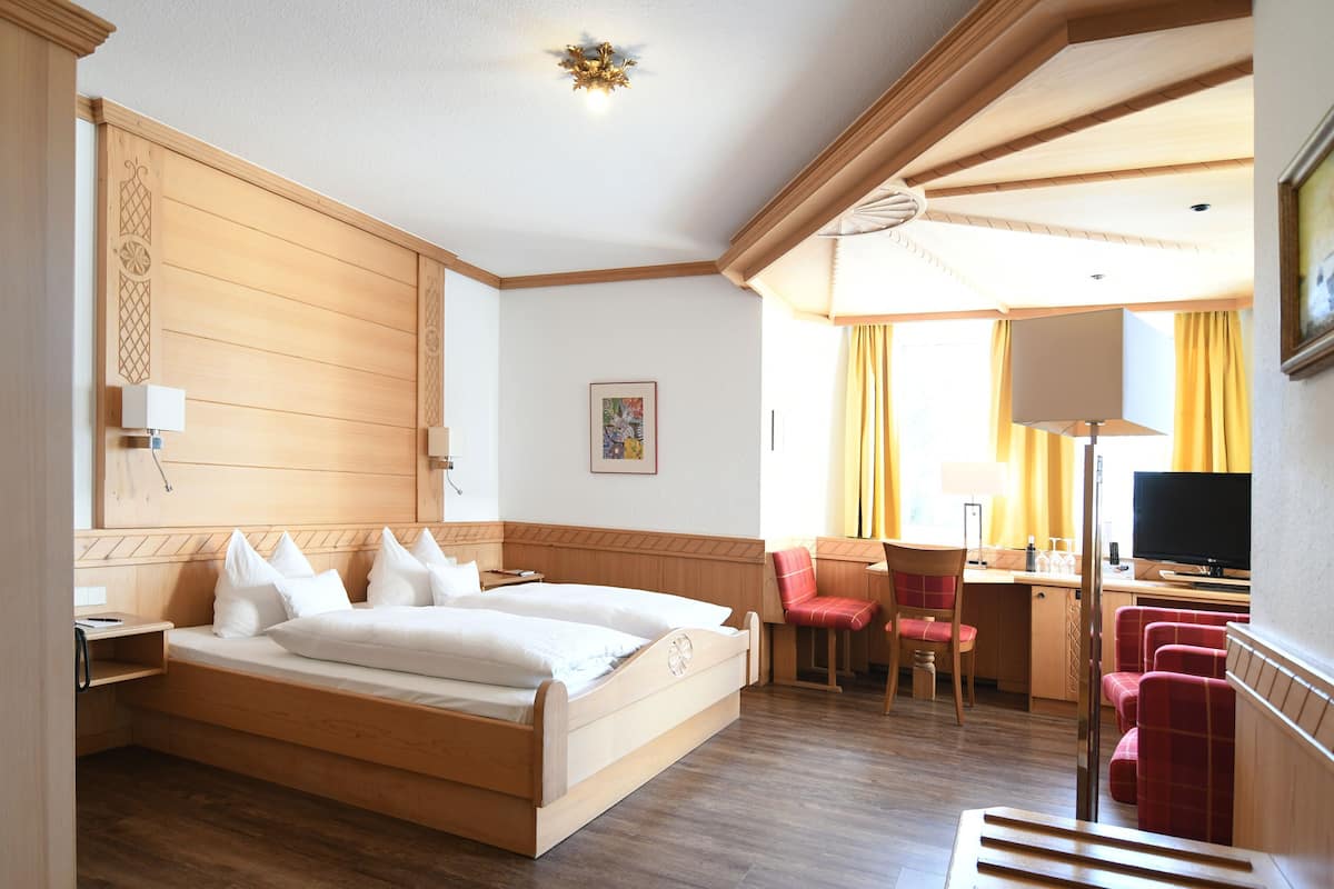 Una habitación de hotel con una cama de madera, un escritorio con una silla, un televisor y una ventana con cortinas.