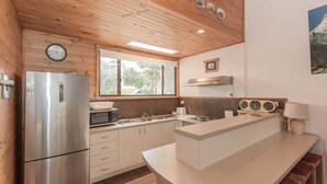 A modern kitchen with a stainless steel refrigerator, a microwave, a sink, and a built-in oven. There is a window above the sink, and a clock on the wall.
