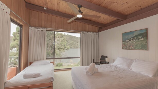 A bedroom with two beds, a ceiling fan, a painting, and a view of a lake.