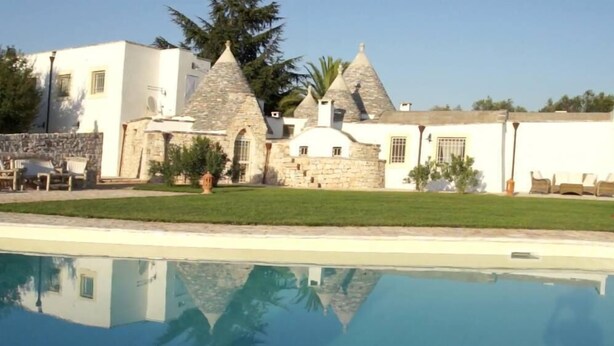 Eine Villa mit Swimmingpool, Steintürmen und einem gepflegten Rasen.