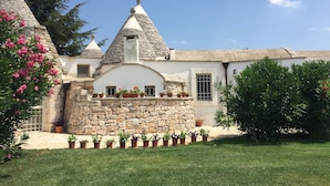 Ein traditionelles Steinhaus mit Kegeldächern, einer Steinsäule und einem gepflegten Garten mit Blumentöpfen.
