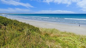 Uma praia com uma pessoa caminhando, dunas gramadas e o oceano.