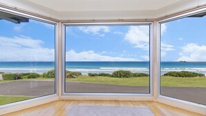 Quarto com janelas amplas que oferecem vista para o oceano e uma área gramada.