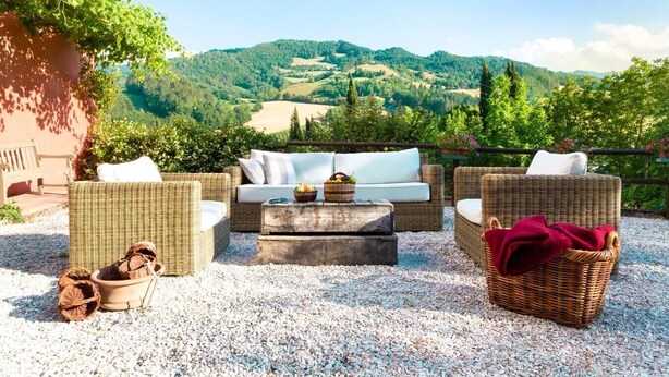 Um terraço com móveis de vime, uma mesa de pedra e vista para colinas ondulantes.
