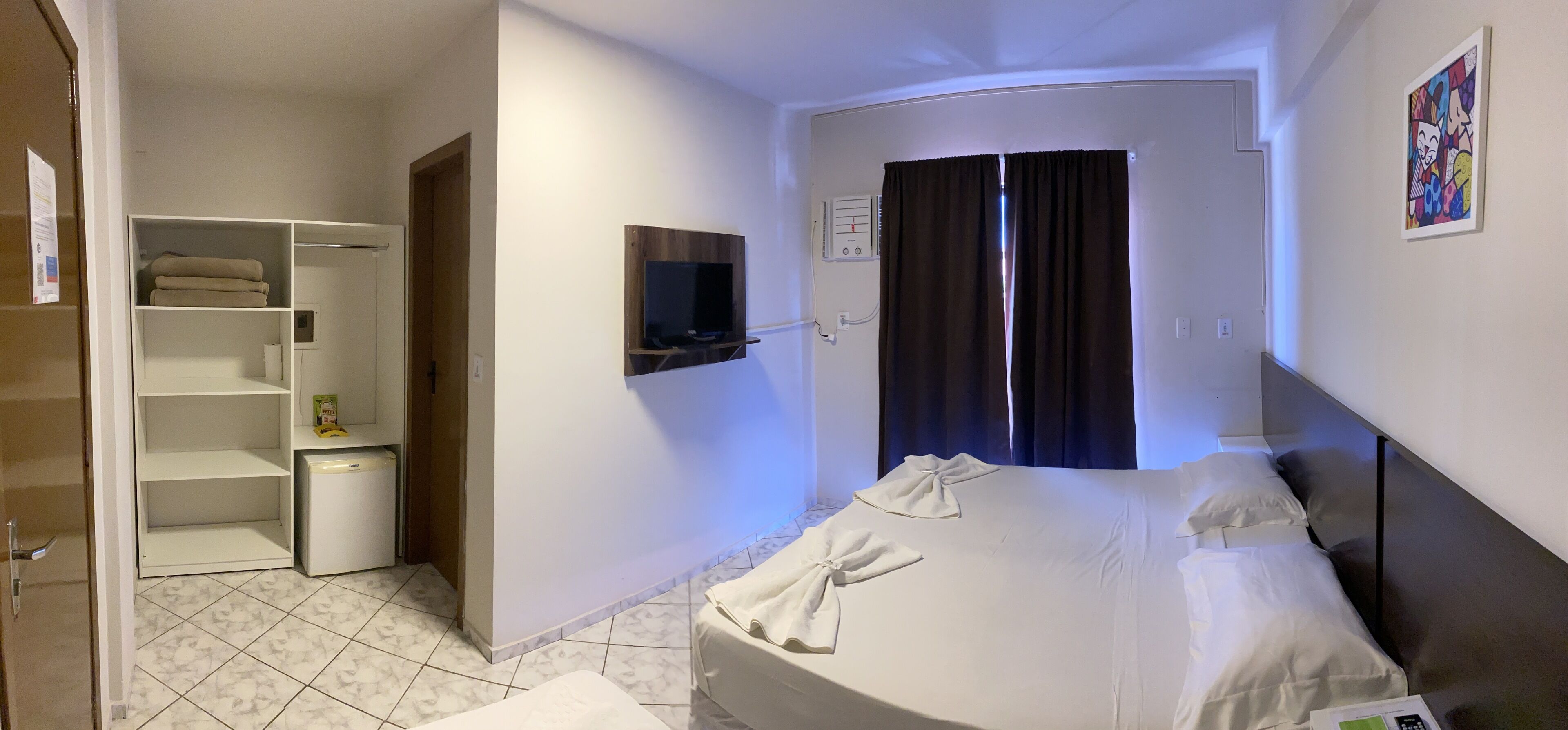 Habitación de hotel con cama, televisor montado en la pared, armario y baño visible a través de una puerta abierta.