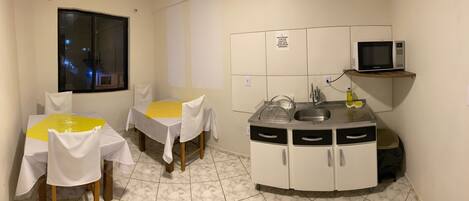 Cocina compacta con microondas, lavabo y armarios de almacenamiento. Hay dos mesas de comedor con sillas, y una ventana con vistas al exterior.