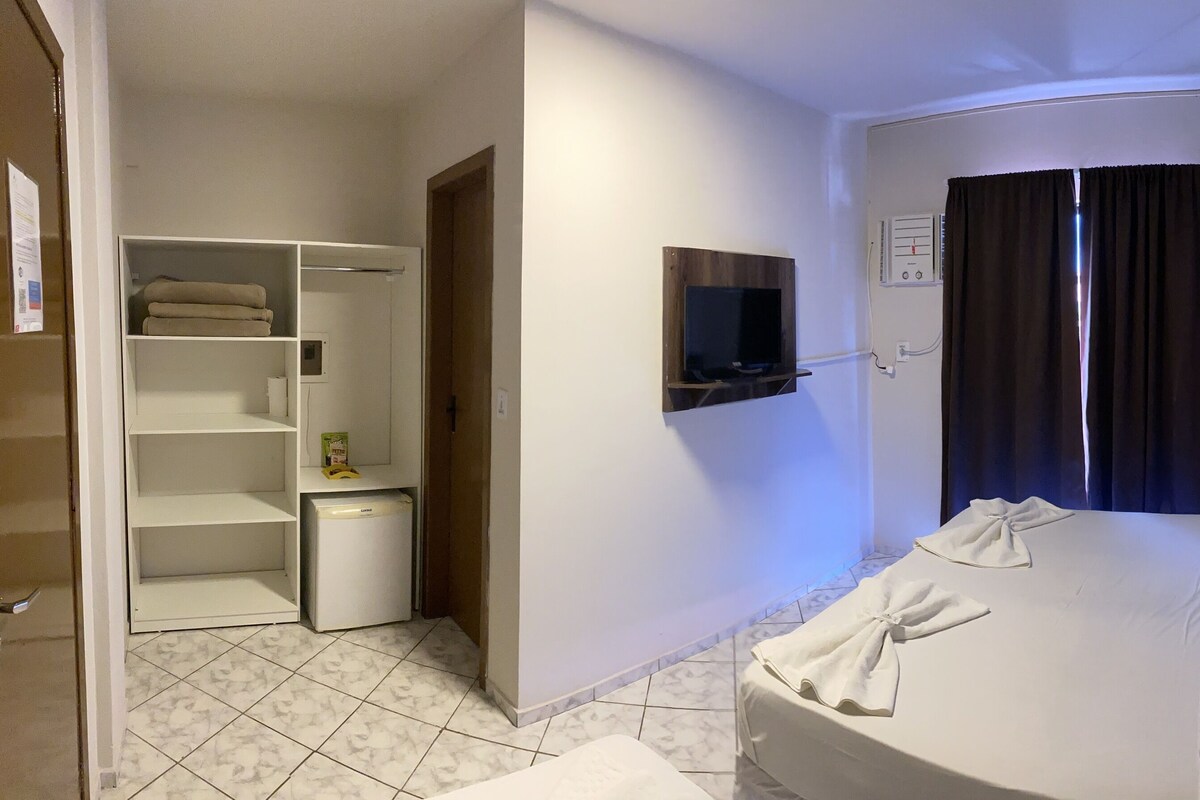 A hotel room with a bed, a TV mounted on the wall, a wardrobe, and a bathroom.