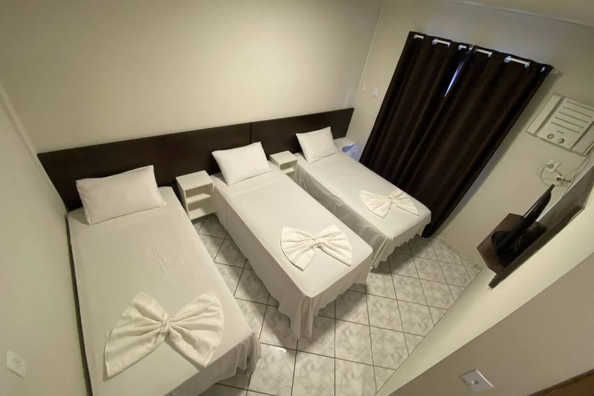 A hotel room with three single beds, each with a bow-tie decoration, a small table, and a TV on the wall.