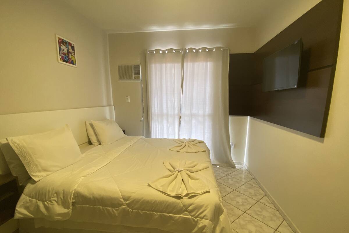 A hotel room with a bed, a TV mounted on the wall, and a window with curtains.