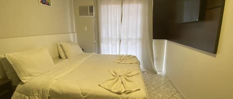 A hotel room with a bed, a TV mounted on the wall, and a window with curtains.