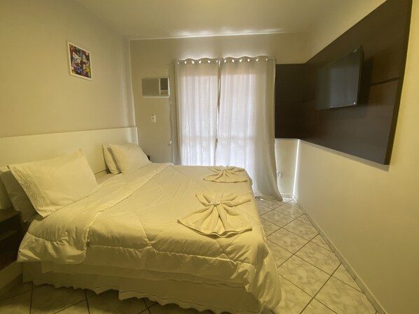 Una habitación de hotel con una cama, un televisor montado en la pared y un ventanal con cortinas.
