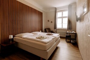 A hotel room with a large bed, a desk, a chair, a radiator, and a window with curtains. - Hotel Ratsstuben Kalbe (Kalbe)