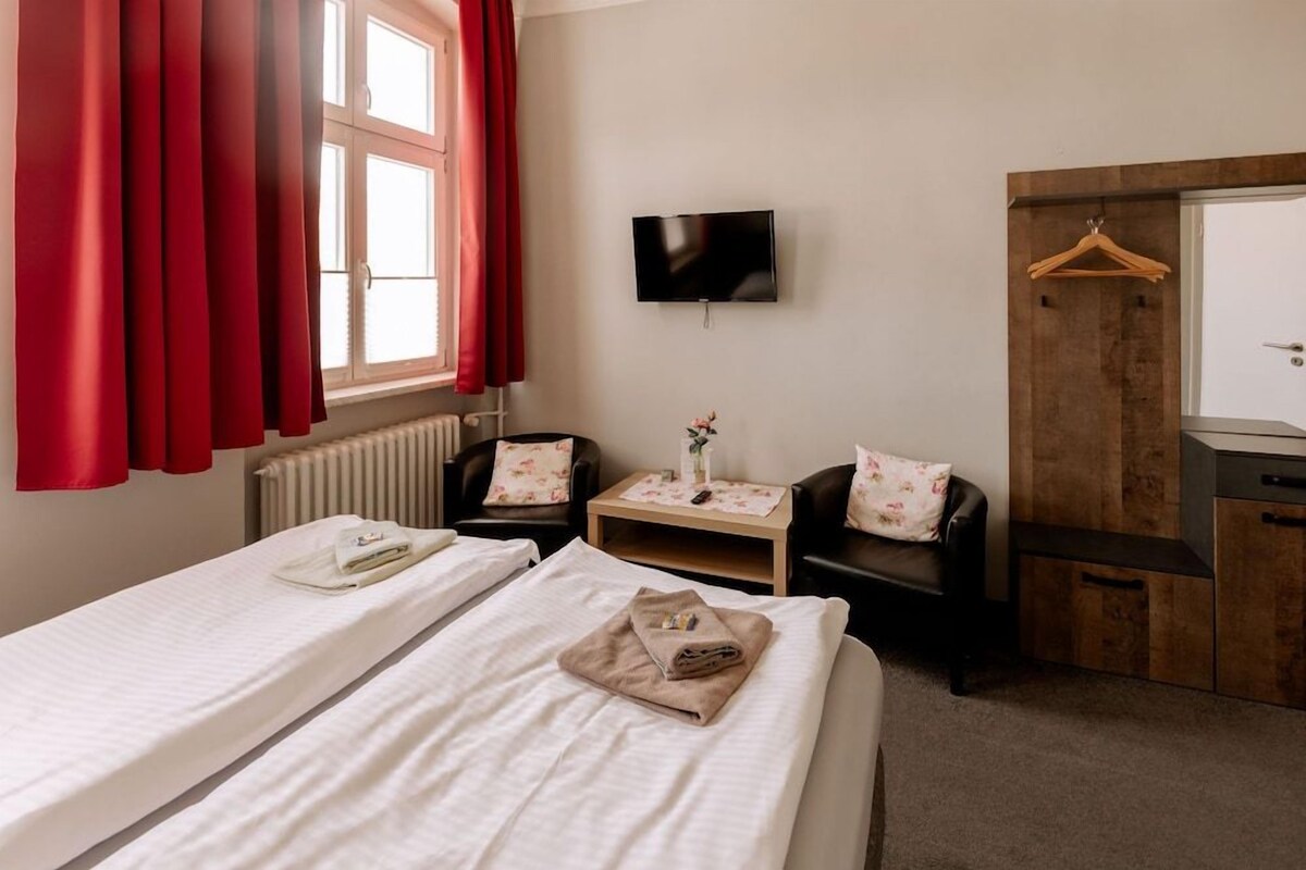 A hotel room with two beds, a TV, a wooden wardrobe, and a small table with a vase.