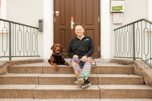 A person sitting on outdoor steps with a dog, a brown door, and a metal railing. - Hotel Ratsstuben Kalbe (Kalbe)