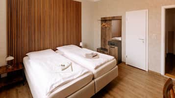 Habitación de hotel con pared de listones de madera, cama con ropa blanca, mesita de noche con lámpara, cómoda y una puerta.