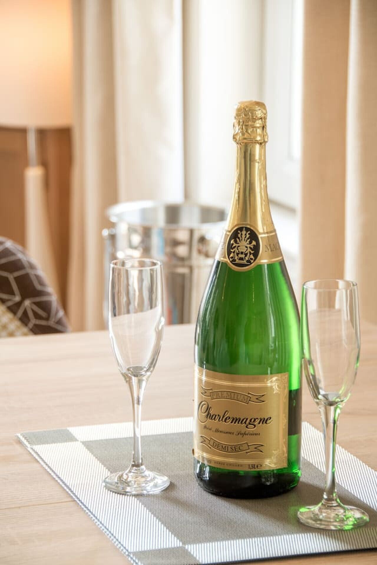 A bottle of Champagne and two glasses on a table with a placemat.