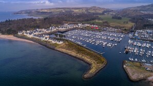 An aerial view of a marina with numerous boats docked, a large building complex, and a coastal landscape. - Marina View Apartment (Inverkip)