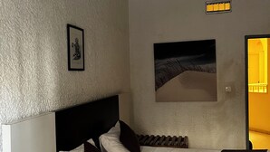 A bedroom with a bed, a nightstand, a framed picture, a wall-mounted light fixture, and a painting. - Maison D'hote O Panoramic (Dakar)