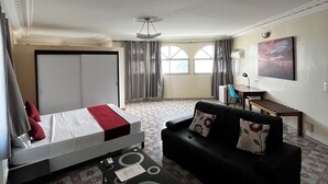 A modern hotel room with a bed, a black sofa, a small table, and a desk with a chair. - Maison D'hote O Panoramic (Dakar)