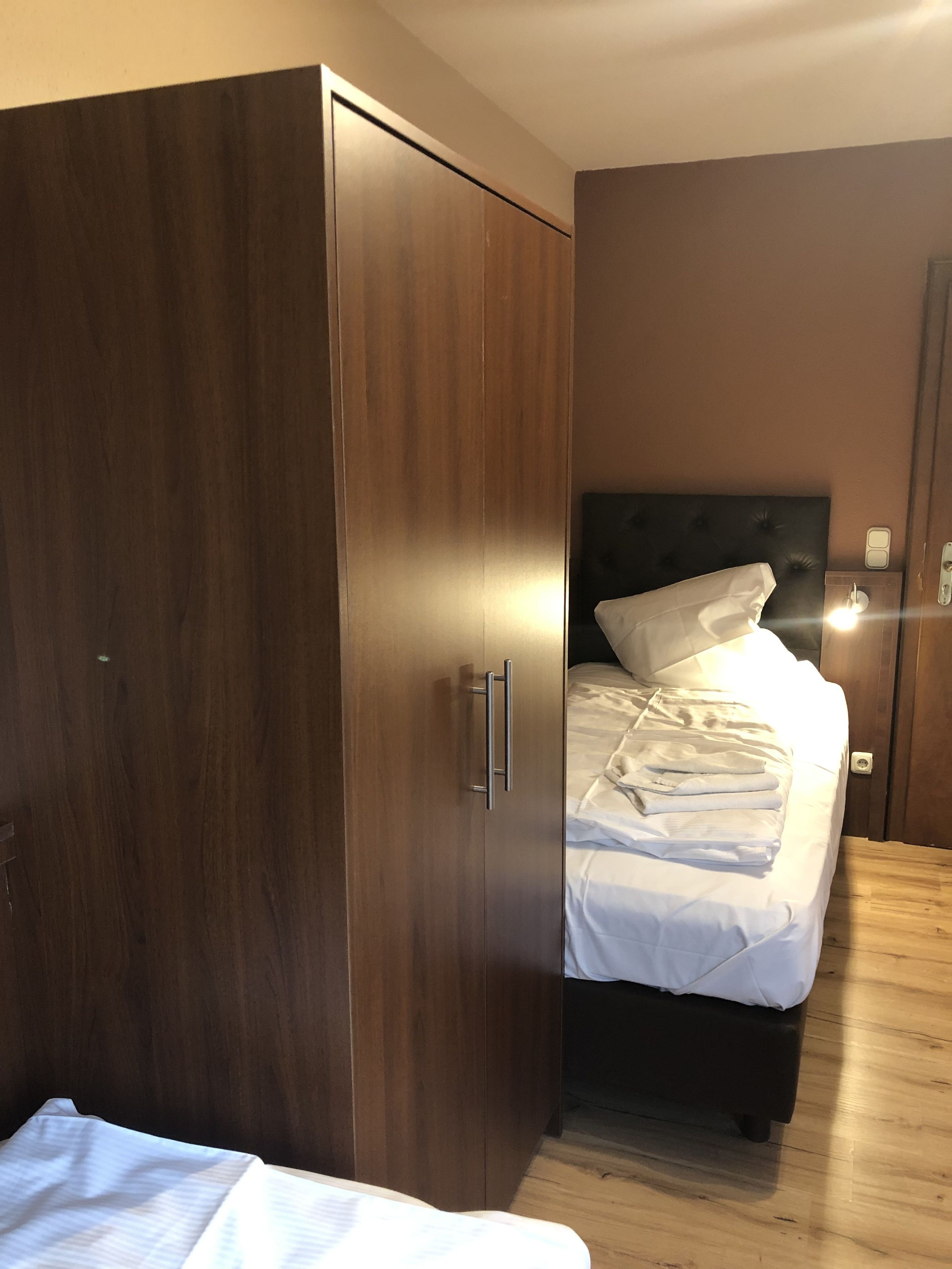 Un dormitorio con un armario de madera, una cama con ropa de cama blanca y una mesita de noche.