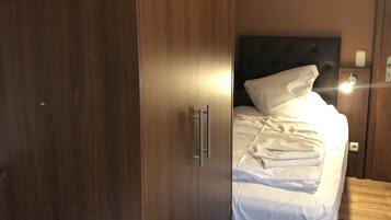 Un dormitorio con un armario de madera, una cama con ropa de cama blanca y una mesita de noche.