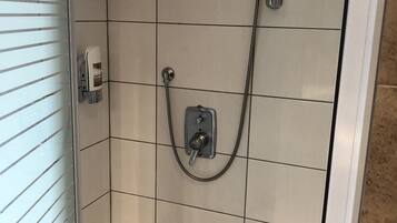 A shower with a handheld showerhead and a wall-mounted control panel.