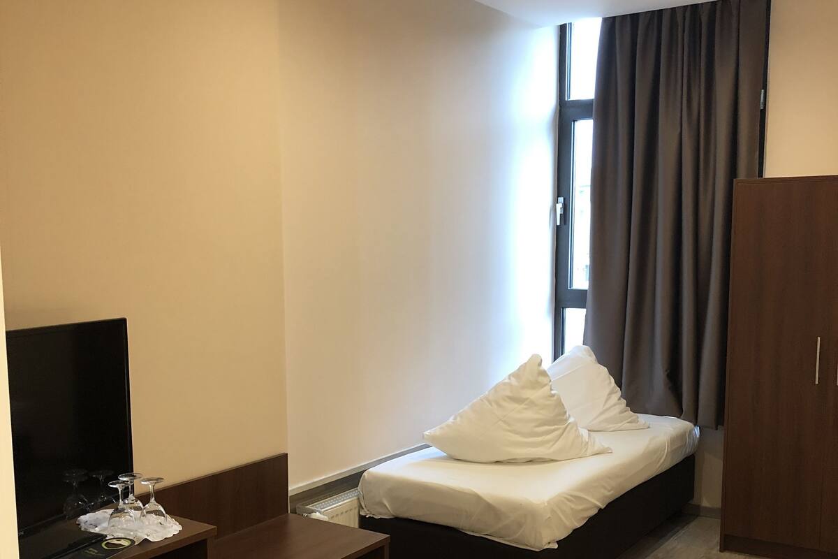 Une chambre d’hôtel avec un lit, un bureau avec une télévision et une fenêtre avec des rideaux.